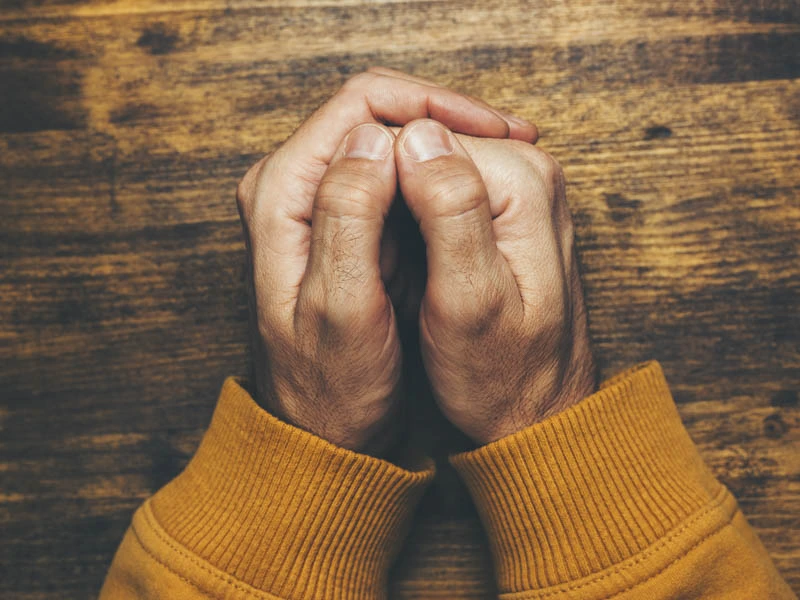 Dłonie złożone w modlitwie na drewnianym stole, symbolizujące osobistą decyzję, wiarę i moment zawierzenia Bogu